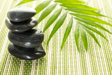 Stack of black basalt balancing stones with green leaf on bamboo mat