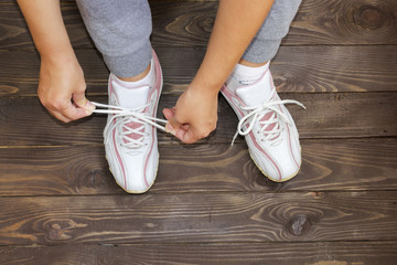 Tying Shoe laces girl sitting on the wooden floor.  White sneakers on a dark wooden background.The view from the top.