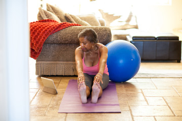 Woman on yoga mat using digital tablet, stretching