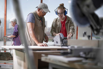 Female trainee carpenter learning to use power saw in furniture making workshop