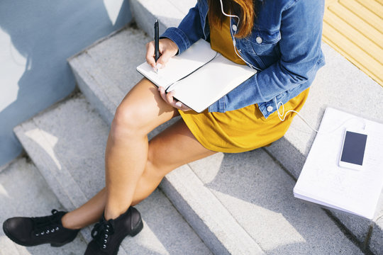 Young woman sitting on steps writing down something, partial view