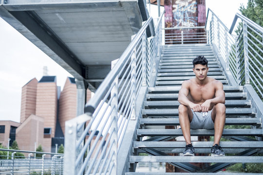 Young man with bare chest sitting on stairs