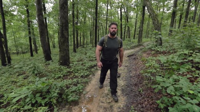 A male hiker walking through woods in shallow focus and slow motion.