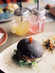 Black craft burger with bacon and rustic drinks on table in cafe