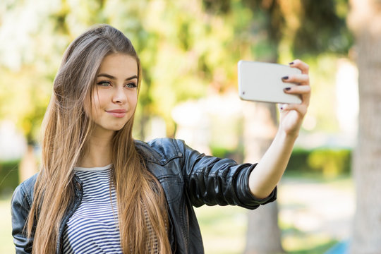 Beautiful blonde teenage girl taking a selfie on smart phone in park