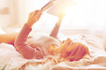 young woman reading book in bed at home