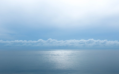 Sun reflecting on sparkling blue sea with soft cloud