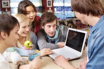 Five students sitting in cafe and watching something on laptop online