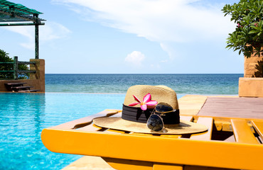 Sunglasses and hat and swimming pool with flower and the sea