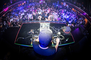 Male DJ performing for crowded nightclub, shot from behind with a fisheye lens