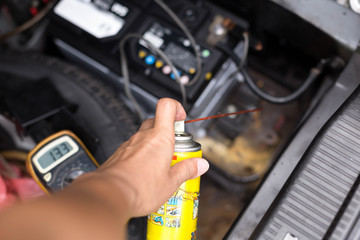 Mechanic holding aerosol cans spray oil for battery replacement