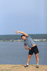 Male runner doing stretching exercise, preparing for morning workout in the park