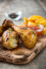 Roast chicken drumsticks with chips on wooden background
