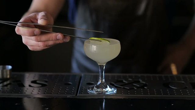 The hands of the bartender garnish the cocktail with lime