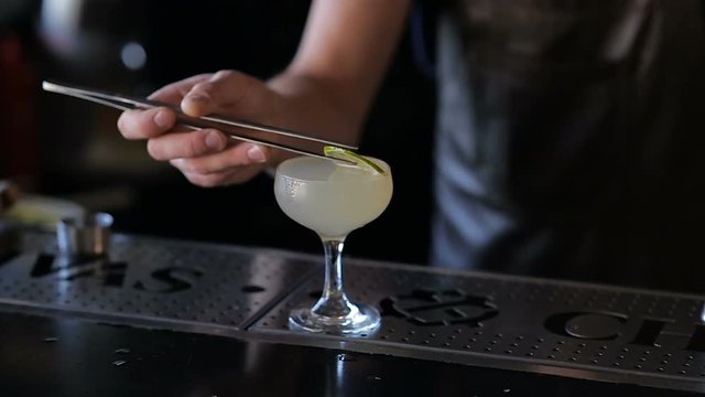 The hands of the bartender garnish the cocktail with lime