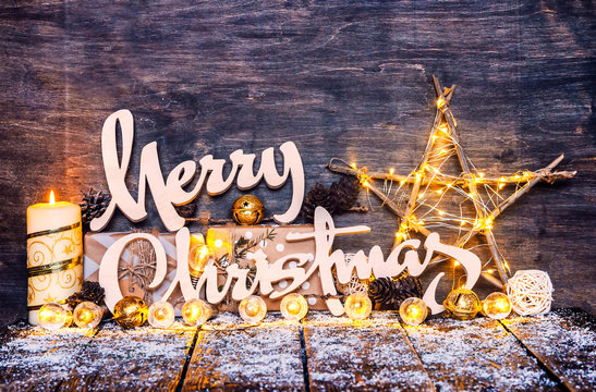 Merry Christmas Background, Fairy Lights,Wood craft rustic Xmas background with wooden letters standing in snow with a star and candle.Wood Crafts With Ornaments.Gifts in Boxes.