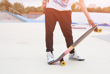 Young man holding a longboard hand on a warm summer evening. Skateboard ramp