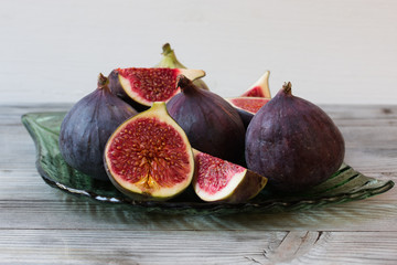 Whole and sliced figs on glass plate. Wooden background. Selective focus.