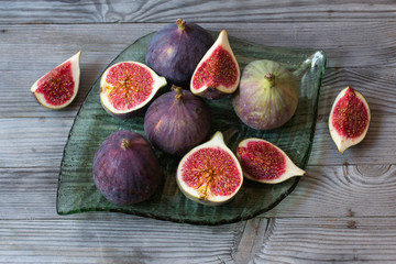 Whole and sliced figs on glass plate. Wooden background. Selective focus.