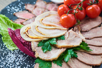 Cold cuts of roast beef, baked ham, chicken roll and beef tongue served on a stone Board
