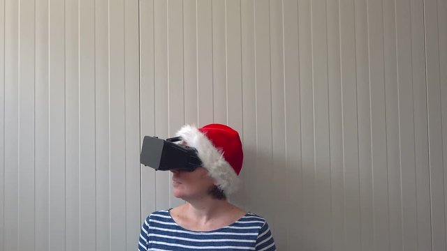 Woman with Christmas Santa Claus hat and VR headset goggles enjoying 360 view video and virtual reality multimedia content.