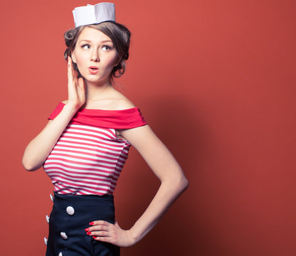 Beautiful pin-up girl dressed a sailor posing on red background