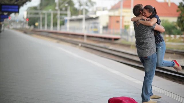 Young couple happy to meet again in the train station, girl runs to meet her boyfriend and throws a suitcase, twist on hands