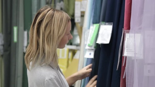 Pretty, young woman choosing curtains in shop