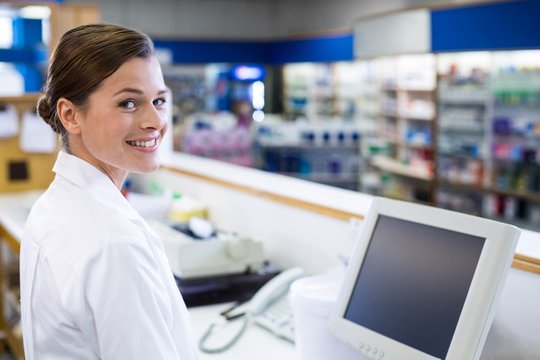 Smiling pharmacist standing at counter in pharmacy