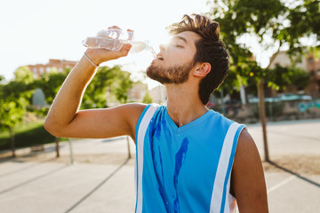 Portrait of handsome young man drinking water on court.