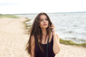 Portrait of young beautiful pretty girl with long brunette hair looking and camera and posing at beach