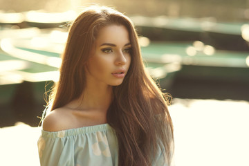 Portrait of young cute woman looking away and posing outdoors in sunset light against bokeh...