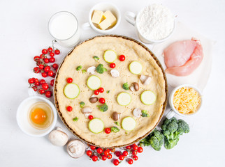 The selection of ingredients for the preparation of traditional French dishes quiche lorraine, on white wooden table with a baked dough in the baking dish in the cooking process, top view, copy space