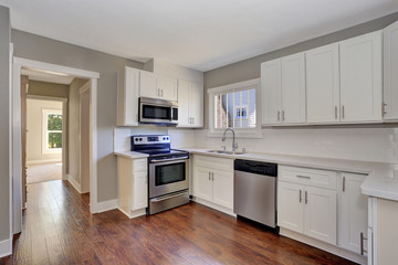 White kitchen room interior with marble counter top and hardwood floor.