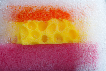 Cleaning yellow orange sponge with soap foam on top. Macro view bubble suds, gray black background.