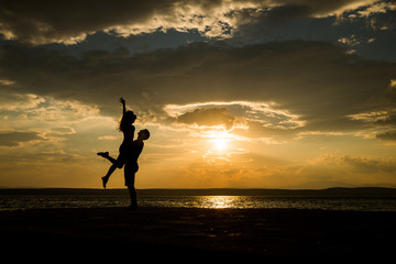 Couple kissing on the beach with a beautiful sunset in background, man lifting the woman