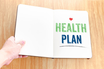 Hand holding notebook with Health plan word lay it on wooden tab
