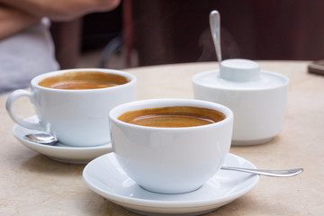Two white cups of coffee, sugar bowl on marble table