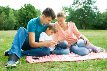 Family Using Digital Tablet In The Park