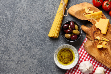 Italian food ingredients stone background with raw spaghetti, olives, parmesan cheese, garlic, olive oil and tomatoes.