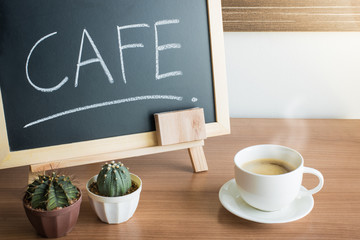 A cup of coffee and cactus with Blackboard Menu frame on wooden Table in cafe