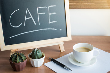A cup of coffee and cactus with Blackboard Menu frame on wooden Table in cafe