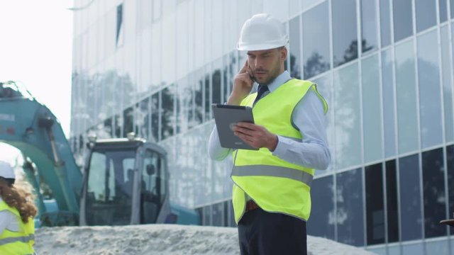 Engineer in Hard Hat Talking on the Phone, Holding Tablet Computer in his Hand. Glass Building under Construction on Background. Shot on RED Cinema Camera in 4K (UHD).