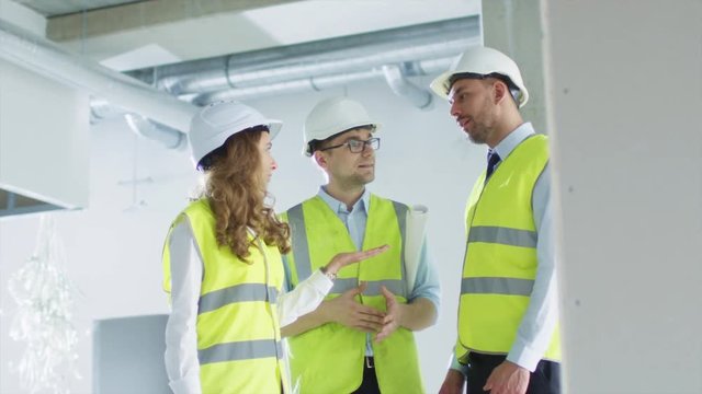 Team of Engineers in Hard Hats Having Conversation, Looking at Blueprint, inside Building Under Construction. Shot on RED Cinema Camera in 4K (UHD).