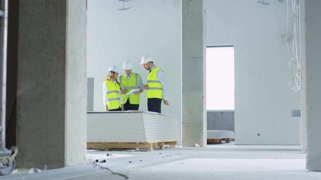 Team of Engineers in Hard Hats Having Conversation, Looking at Blueprint, inside Building Under Construction. Shot on RED Cinema Camera in 4K (UHD).