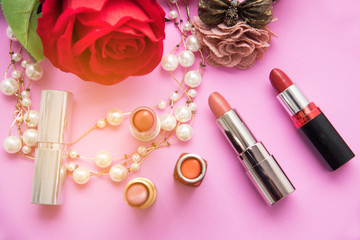 Decorative flat lay composition with colorful lipstick , pearl and flowers. Top view on pink background.