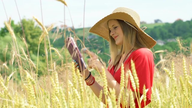 Girl browsing internet on tablet and smiling to the camera in the grain field

