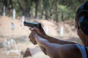 Male in white sleeveless shirt firing pistol at shooting range - obrazy, fototapety, plakaty
