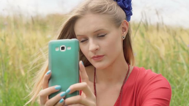 Pretty girl doing selfies on smartphone while sitting in the grain field
