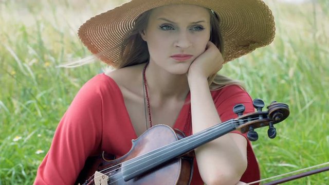 Unhappy girl holding violing and sitting on the field
